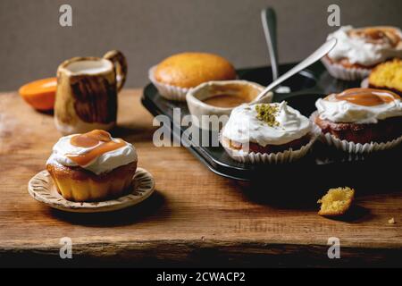 Oranges d'agrumes ou clémentines maison muffins doux cupcakes dans un plateau cuit avec différentes crèmes, pistaches, garnitures de caramel dans des bols au-dessus de bois Banque D'Images