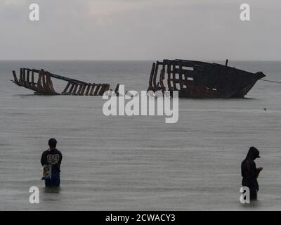 Vue sur les silhouettes d'un bateau détruit et d'un pêcheur durant la marée haute sur la mer de Saram. Temps pluvieux. Kaimana, Péninsule De Bird'S Head, Pa Occidentale Banque D'Images
