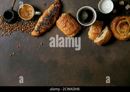 Variété de pains à base de raisins secs et de chocolat, croissant avec différentes tasses de café et de lait, cizve, cuillère en bois recyclé Banque D'Images