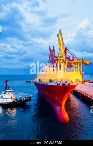 Remorqueur pousser le grand cargo pour l'accostage au terminal du port. Fonctionnement du terminal portuaire et équipement de manutention. Banque D'Images