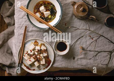 Soupe japonaise au bouillon Miso avec cubes de tofu en soie, haricots de soja edamame, haricots verts dans un bol traditionnel avec baguettes, théière en céramique et tasses sur lin gris Banque D'Images