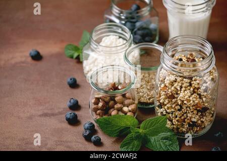 Granola de grain de millet croustillant maison avec fruits secs et noix, yaourt, lait, muesli dans différents pots de verre, menthe. Fond marron. Santé Banque D'Images