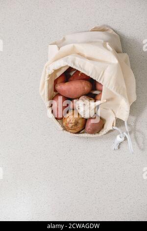 Variété de légumes frais biologiques pommes de terre, oignon et ail dans le sac à provisions en coton blanc. Écologique, zéro gaspillage. Arrière-plan de texture grise. Banque D'Images
