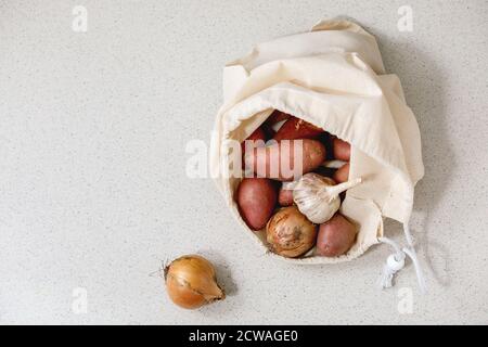 Variété de légumes frais biologiques pommes de terre, oignon et ail dans le sac à provisions en coton blanc. Écologique, zéro gaspillage. Arrière-plan de texture grise. Banque D'Images