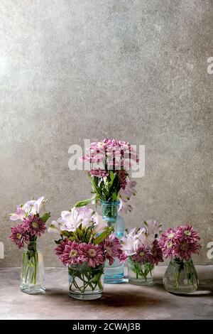 Groupe de bouteilles en verre et vases avec bouquets de fleurs décoratives roses sur fond de texture grise. Banque D'Images