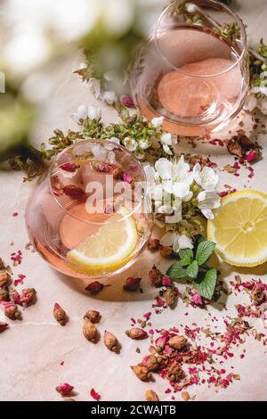 Verres à cocktail de champagne rose, de cidre ou de limonade avec boutons de rose secs, citron et menthe. Des branches de cerisier fleurient au-dessus. Fond en marbre rose. Banque D'Images