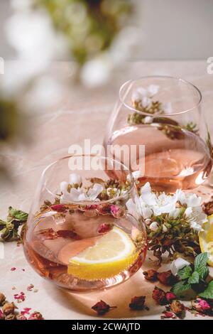 Verres à cocktail de champagne rose, de cidre ou de limonade avec boutons de rose secs, citron et menthe. Des branches de cerisier fleurient au-dessus. Fond en marbre rose. Banque D'Images