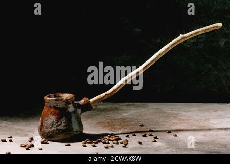 Café turc noir dans une cafetière artisanale en céramique avec une longue poignée en bois et des grains de café au-dessus. Fond de texture gris. Copier l'espace Banque D'Images