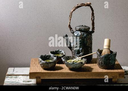 Thé vert matcha japonais dans des tasses en céramique artisanale avec poudre de matcha, fouet en bambou, théière en céramique sur table japonaise traditionnelle en bois. Banque D'Images