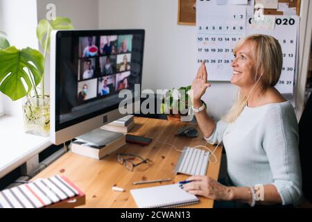 Femme mûre souriante ayant des appels vidéo via l'ordinateur le bureau à domicile. Vidéoconférence en ligne pour les réunions d'équipe depuis la maison. Femme d'affaires attirante Banque D'Images