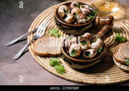 Escargols de Bourgogne - escargots au beurre d'herbes, plat gastronomique, dans deux casseroles traditionnelles en céramique avec coriandre, pain et verre de vin blanc sur la stra Banque D'Images