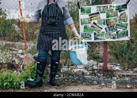 Femme en gants blancs avec des fournitures de nettoyage près d'un dépotoir. Dire non à la pollution de l'environnement. Les parcs d'affiches au lieu des décharges sur la clôture à maillons de chaîne Banque D'Images