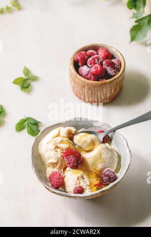 Glace à la vanille au caramel fondu maison avec sirop et framboises congelées dans un bol en céramique placé sur une table en marbre blanc. Banque D'Images