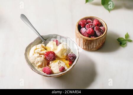 Glace à la vanille au caramel fondu maison avec sirop et framboises congelées dans un bol en céramique placé sur une table en marbre blanc. Banque D'Images