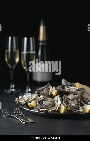 Assiette de coquillages d'huîtres frais ouverts sur glace, deux verres de champagne et une bouteille sur une table blanche. Mise au point sélective Banque D'Images