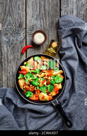 Poulet à la noix de cajou aux légumes sautés : brocoli, poivron, piment rouge chaud et sauce soja servis sur une poêle sur fond de bois rustique, vue du dessus Banque D'Images