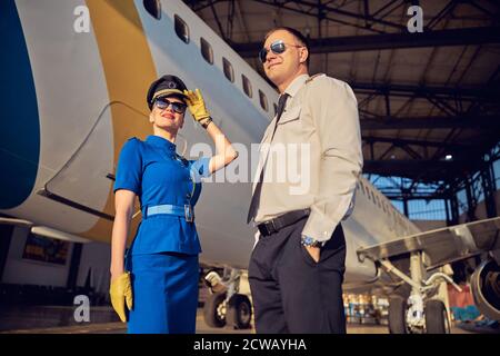 Femme et homme souriants qui portent un uniforme professionnel debout garage d'aviation Banque D'Images