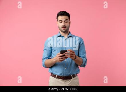 jeune homme décontracté tenant le téléphone et lisant les nouvelles, debout sur fond rose Banque D'Images