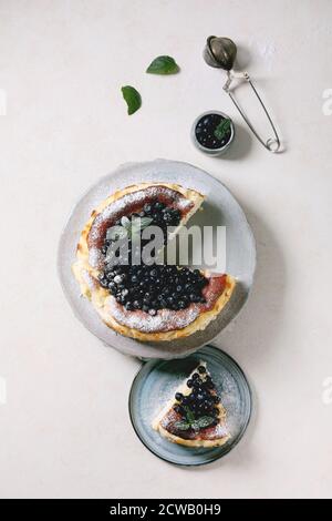 Gâteau au fromage doux au myrtille maison san sebastian, entier et coupé en tranches, sur plaque en céramique décorée de baies sauvages fraîches, de sucre glace et de menthe Banque D'Images