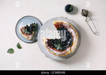 Gâteau au fromage doux au myrtille maison san sebastian, entier et coupé en tranches, sur plaque en céramique décorée de baies sauvages fraîches, de sucre glace et de menthe Banque D'Images