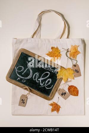 Concept de vente d'automne. Tableau noir vintage avec lettrage écrit à la main solde, étiquettes avec des percents, feuilles jaunes d'automne sur sac de shopping en lin écologique plus d'être Banque D'Images