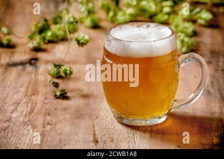 Tasse en verre classique de bière blonde fraîche avec des cônes de houblon verts sur fond de texture en bois. Copier l'espace Banque D'Images