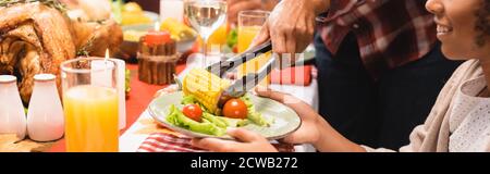 vue rognée de la mère mettant du maïs sur l'assiette pour fille afro-américaine pendant le dîner d'action de grâce, photo panoramique Banque D'Images