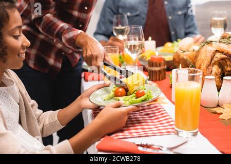 concentration sélective de la femme afro-américaine mettant du maïs sur plaque pour la fille pendant le dîner de thanksgiving Banque D'Images