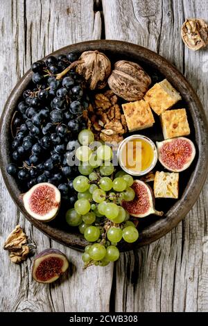 Hors-d'œuvre au vin avec différents raisins, figues, noix, pain, miel et fromage de chèvre sur plaque de céramique sur fond de bois ancien. Flat lay, espace de copie Banque D'Images