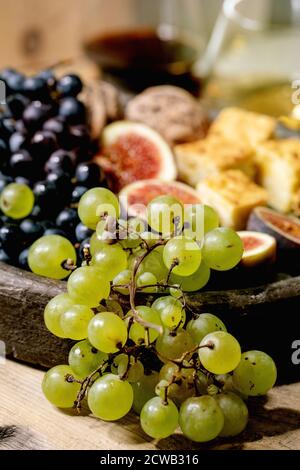 Hors-d'œuvre au vin avec différents raisins, figues, noix, pain, miel et fromage de chèvre sur plaque en céramique, servant avec des verres de vin rouge et blanc sur o Banque D'Images