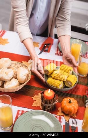 Vue rognée d'une assiette de femme senior avec du maïs table près des décorations de thanksgiving Banque D'Images