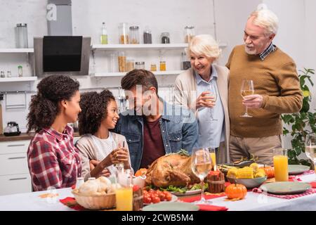 Accent sélectif de la famille multiculturelle célébrant l'action de grâce près de la nourriture sur tableau Banque D'Images