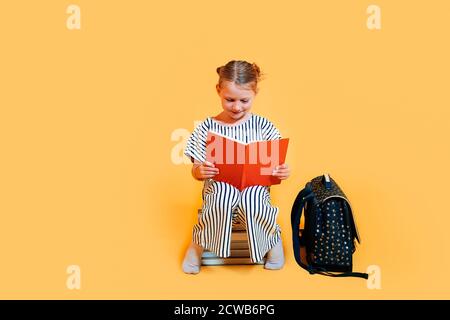 une fille assise à l'école sourit et lit un livre. Apprentissage à l'école concept. Banque D'Images