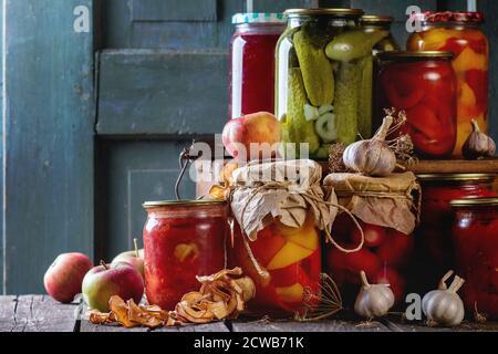 Collection de nombreux pots faits maison en verre avec des aliments conservés (concombres, tomates, poivrons), avec de l'ail et des pommes fraîches et séchées. Sur le vieux bois Banque D'Images