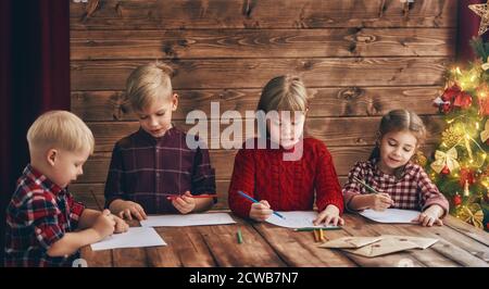 Joyeux Noël et joyeuses fêtes. Groupe de quatre enfants sur fond de bois. Portrait de beaux petits enfants en train d'écrire des lettres au Père Noël Banque D'Images