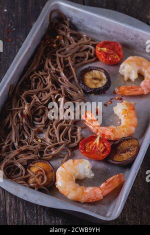 Dîner asiatique avec nouilles soba, champignons shiitake, tomates grillées et crevettes dans un plat à pâtisserie en aluminium sur fond de bois ancien. Rustique foncé Banque D'Images