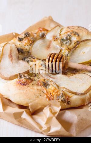 Pizza entière avec poires, gorgonzola et le miel Le miel en bois d'olivier avec balancier sur papier cuisson sur table en bois blanc. Banque D'Images