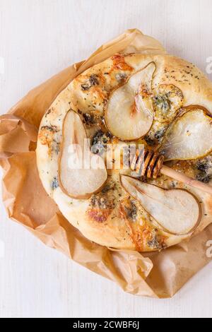 Pizza entière avec poires, gorgonzola et le miel Le miel en bois d'olivier avec balancier sur papier cuisson sur table en bois blanc. Vue d'en haut Banque D'Images