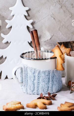 Biscuits de Noël sablés pour tasses, tasse de thé chaud vintage dans un porte-gobelet tricoté, bâtonnets de cannelle et sucre en poudre sur table avec nappe blanche Banque D'Images