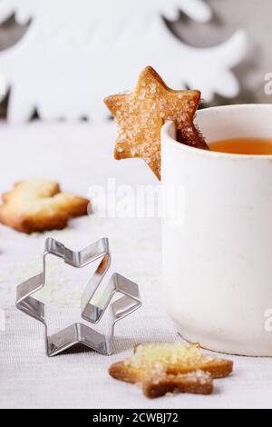 Biscuits de Noël sablés pour tasses, tasse de thé chaud vintage, emporte-pièce, bâtons de cannelle et sucre en poudre sur table avec nappe blanche avec C Banque D'Images