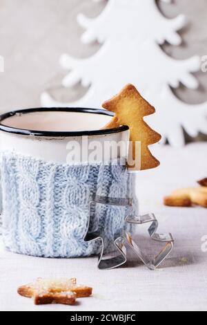 Biscuits de Noël sablés pour tasses, tasse de thé chaud vintage dans un porte-gobelet tricoté, bâtonnets de cannelle et sucre en poudre sur table avec nappe blanche Banque D'Images