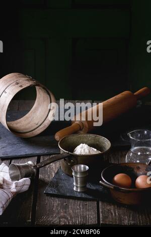 Ingrédients pour la préparation de la pâte. Farine, œufs dans des bols en cuivre d'époque et sel avec tamis et rolling-pin sur une ancienne table en bois. Style rustique. Banque D'Images