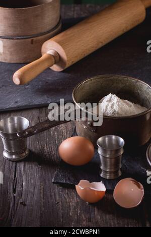 Ingrédients pour la préparation de la pâte. Farine, œufs dans des bols en cuivre d'époque et sel avec tamis et rolling-pin sur une ancienne table en bois. Style rustique. Banque D'Images