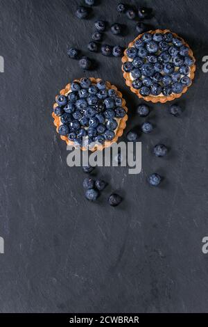 Deux tartelettes au citron avec des bleuets frais sur fond ardoise noire. Vue d'en haut. Avec un espace réservé au texte Banque D'Images