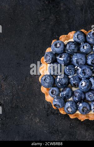 Tartelette au citron avec des bleuets frais sur fond noir. Vue d'en haut. Avec un espace réservé au texte Banque D'Images