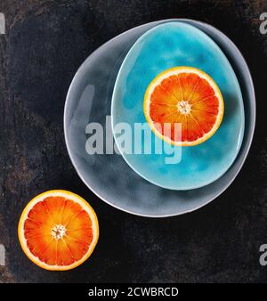 Tranches de fruits orange sanguine sicilienne sur turquoise brillant et plaques en céramique gris sur fond noir. Mise à plat Banque D'Images