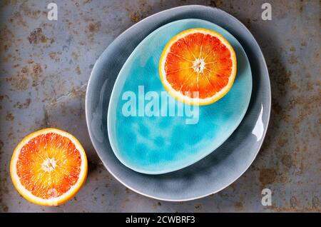 Tranché de fruits orange de sang sicilien sur des plaques de céramique turquoise et grise sur fond de métal rouillé. Pose à plat Banque D'Images