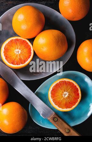 Fruits orange de sang sicilien entiers et tranchés sur des plaques de céramique turquoise et grise sur fond noir, avec couteau vintage. Pose à plat Banque D'Images