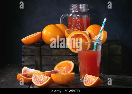 Tout en tranches et d'orange sanguine de Sicile et verre de jus d'orange rouge plus vieille table en bois. Style rustique foncé. Banque D'Images