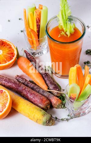 Émincé de carottes et de céleri crus et colorés comme en-cas végétarien, d'oranges sanguines et de thym avec une tasse de verre d'orange frais et de jus de carottes sur la pierre blanche Banque D'Images